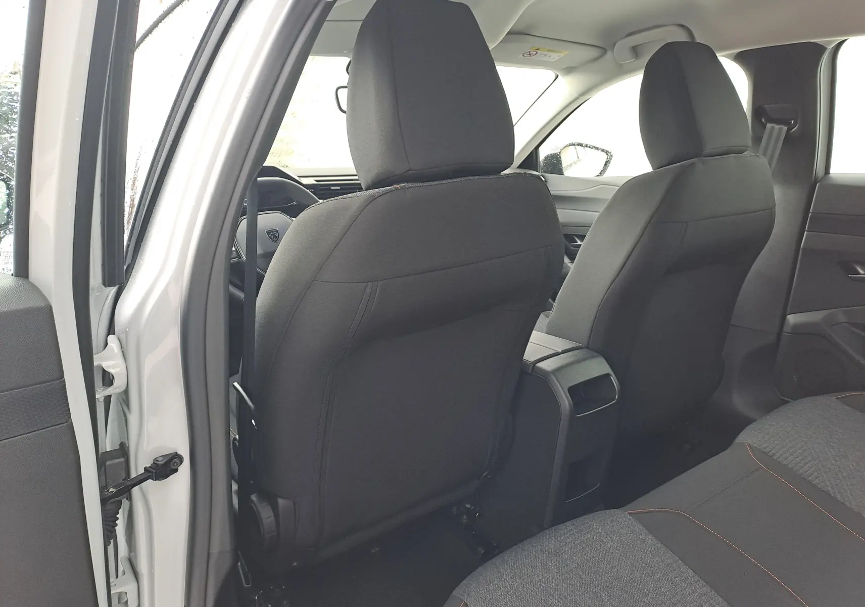 Vue intérieure arrière côté gauche de la Peugeot 308 blanche, montrant les sièges avant noirs et la console centrale.