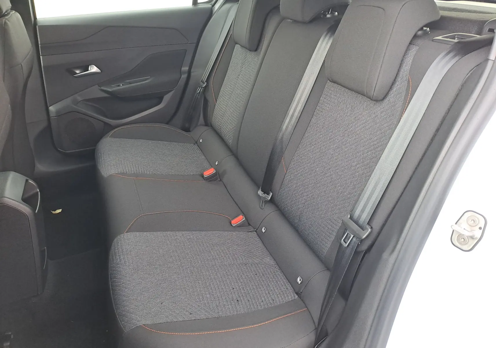 Vue intérieure côté droit des sièges arrière gris foncé avec surpiqûres orange d'une Peugeot 308 blanche 2025.