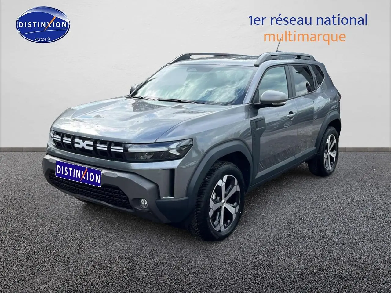 Dacia Duster gris schiste en 3/4 avant droit, avec barres de toit et jantes alliage distinctives.