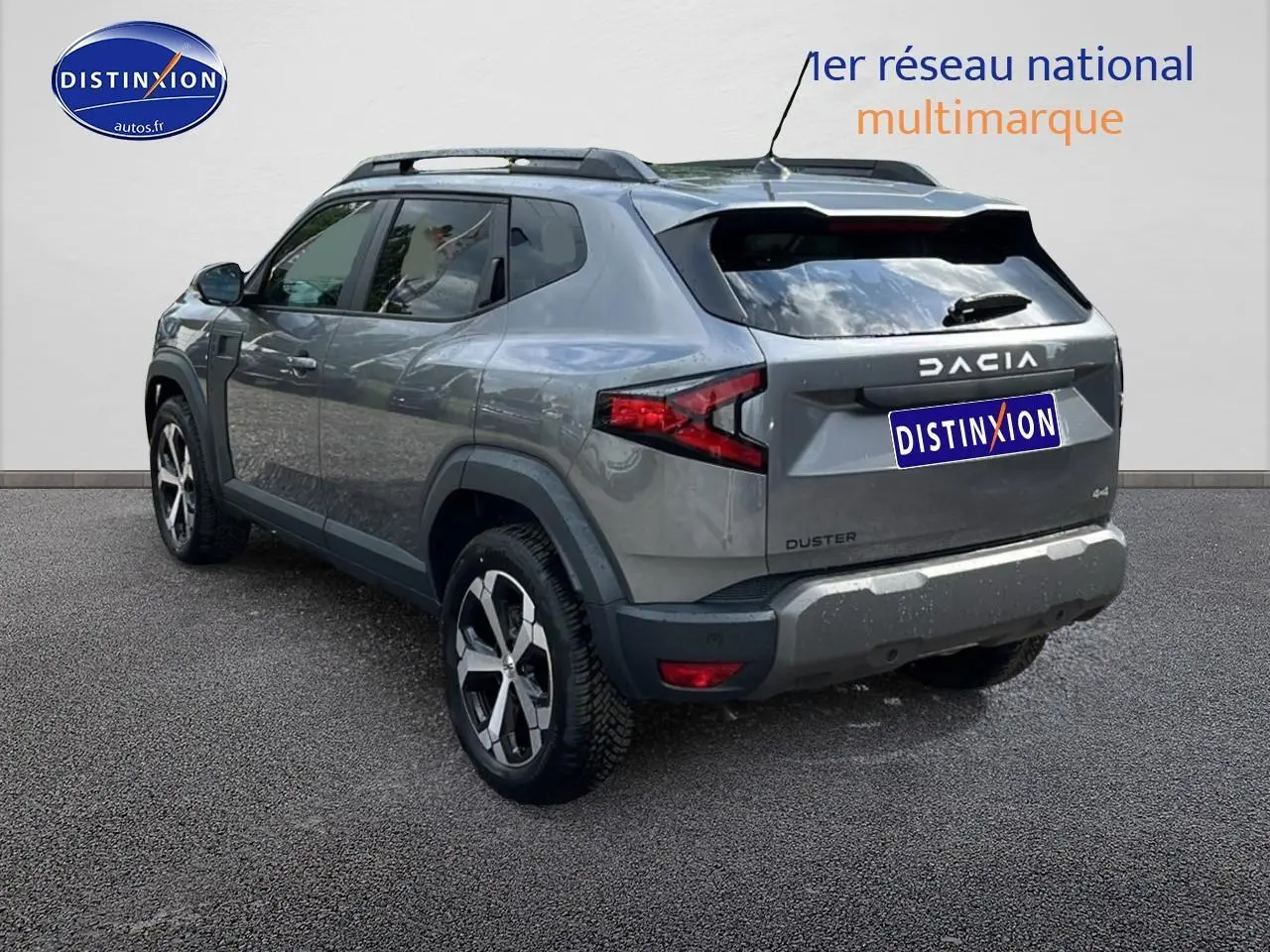 Vue 3/4 arrière droite du Dacia Duster gris schiste avec jantes alu et barres de toit visibles.