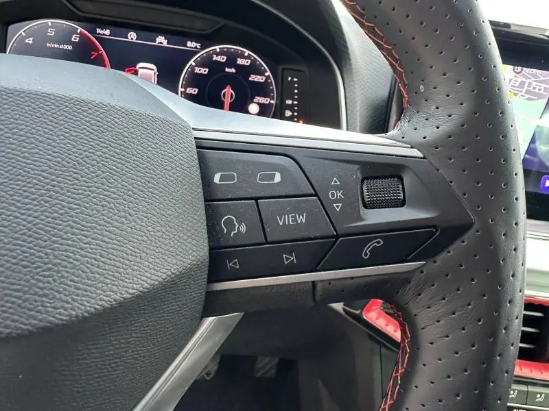 Gros plan sur le volant côté gauche de la SEAT Ibiza 1.0 TSI 115cv FR 2025 avec commandes intégrées et coutures rouges.