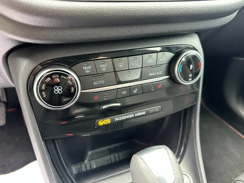 Gros plan sur la console centrale noire du Ford Puma 2024, montrant les commandes de climatisation et les voyants du tableau de bord.