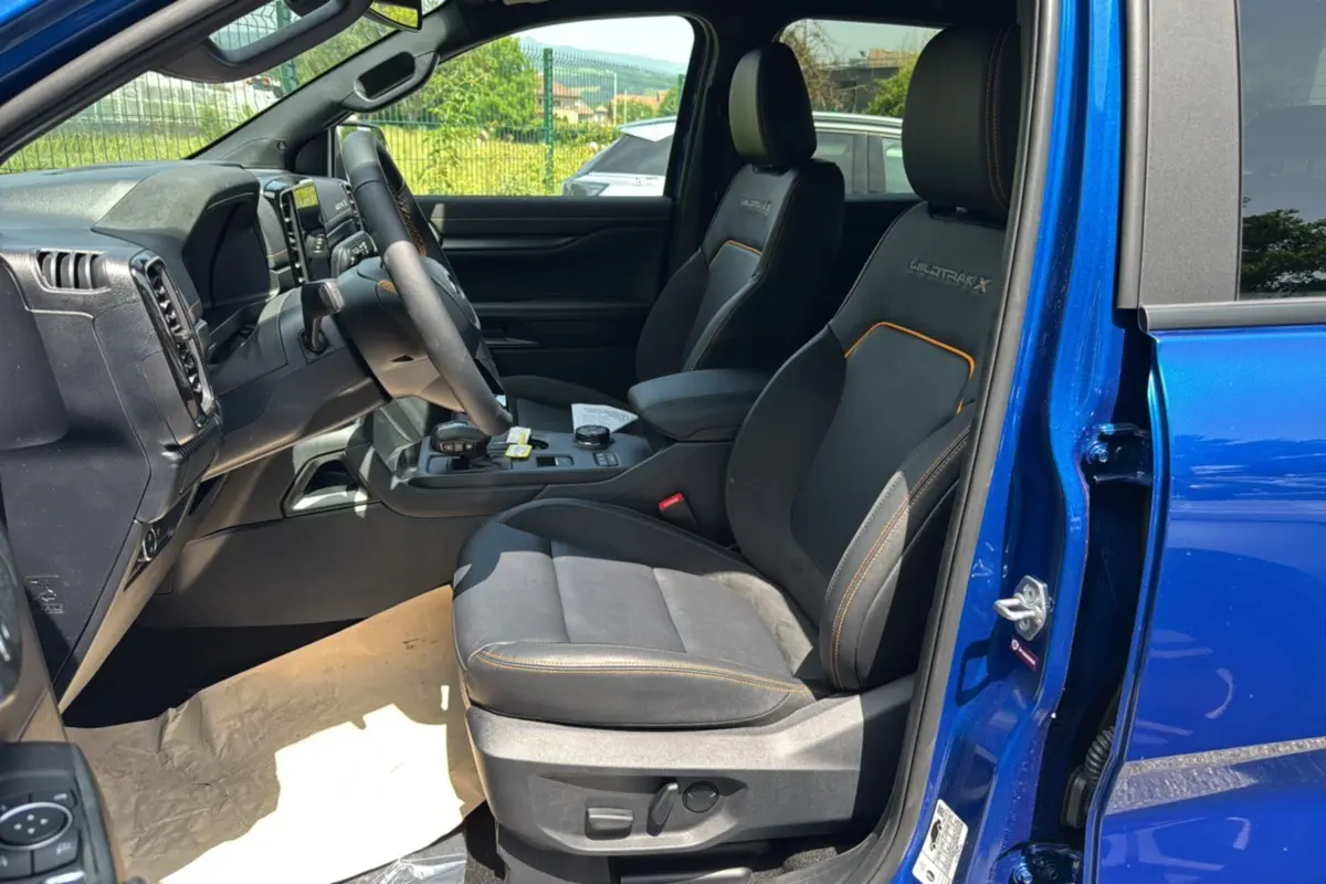 Intérieur côté conducteur du Ford Ranger 205 Wildtrak X bleu Lightning, sièges noirs avec surpiqûres orange et volant cuir multifonctions.