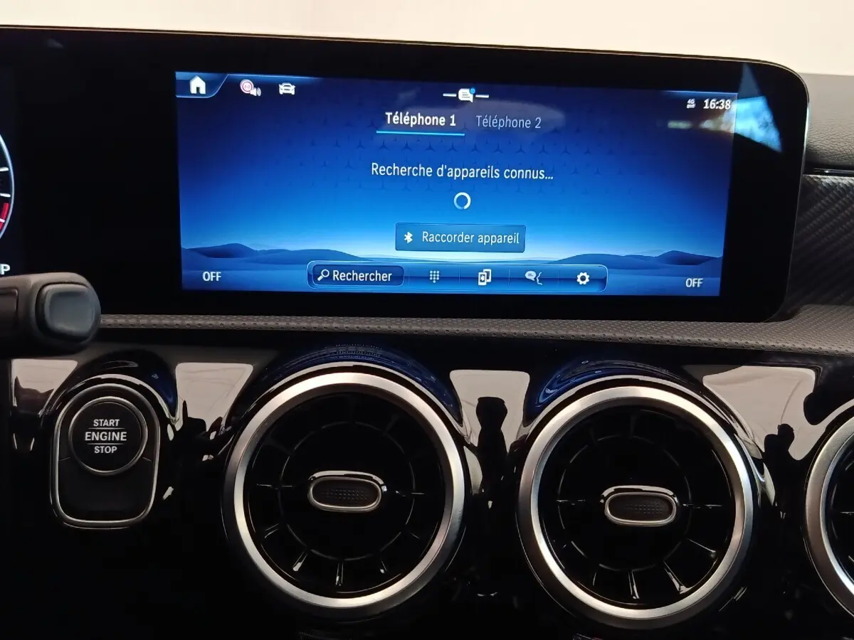 Vue rapprochée du tableau de bord noir brillant de la Mercedes Classe A 250 e Hybrid avec écran tactile bleu et boutons circulaires d’aération.