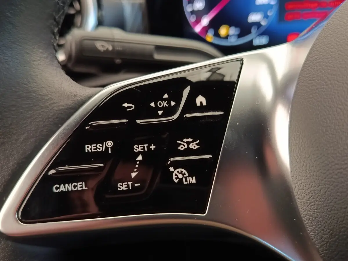 Gros plan sur les commandes multifonctions noires du volant côté gauche d’une Mercedes Classe A 250 e hybride 2024.