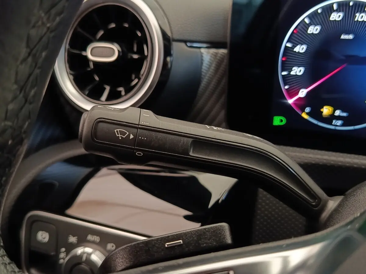 Gros plan sur la manette d’essuie-glace à gauche du volant dans l’habitacle gris foncé de la Mercedes Classe A 250 e Hybrid 2024.