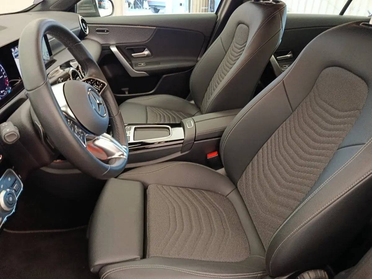 Vue intérieure côté conducteur de la Mercedes Classe A 250 e Hybrid avec sièges noirs et volant cuir multifonctions.