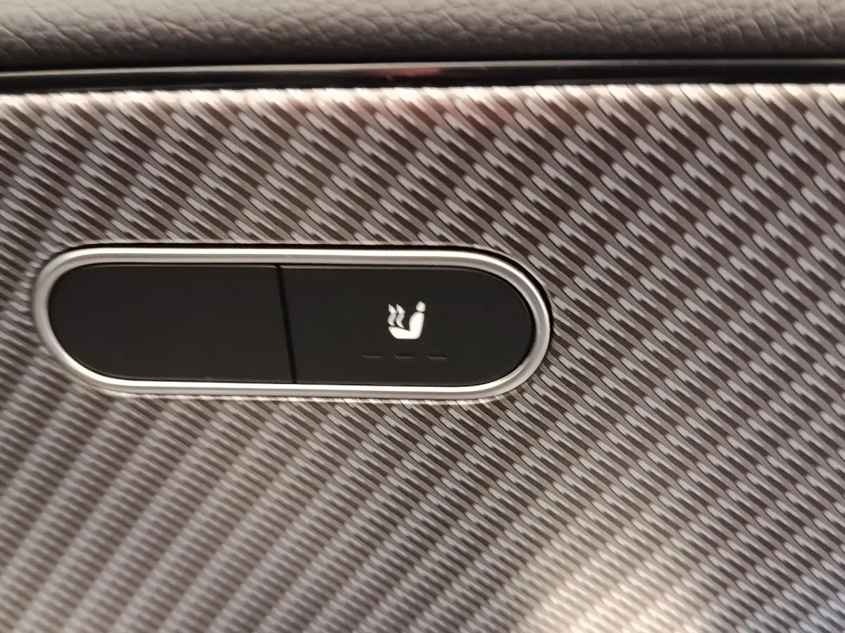 Gros plan sur le bouton de siège chauffant sur une surface à motif carbone à l'intérieur de la Mercedes Classe A 250 e Hybrid.