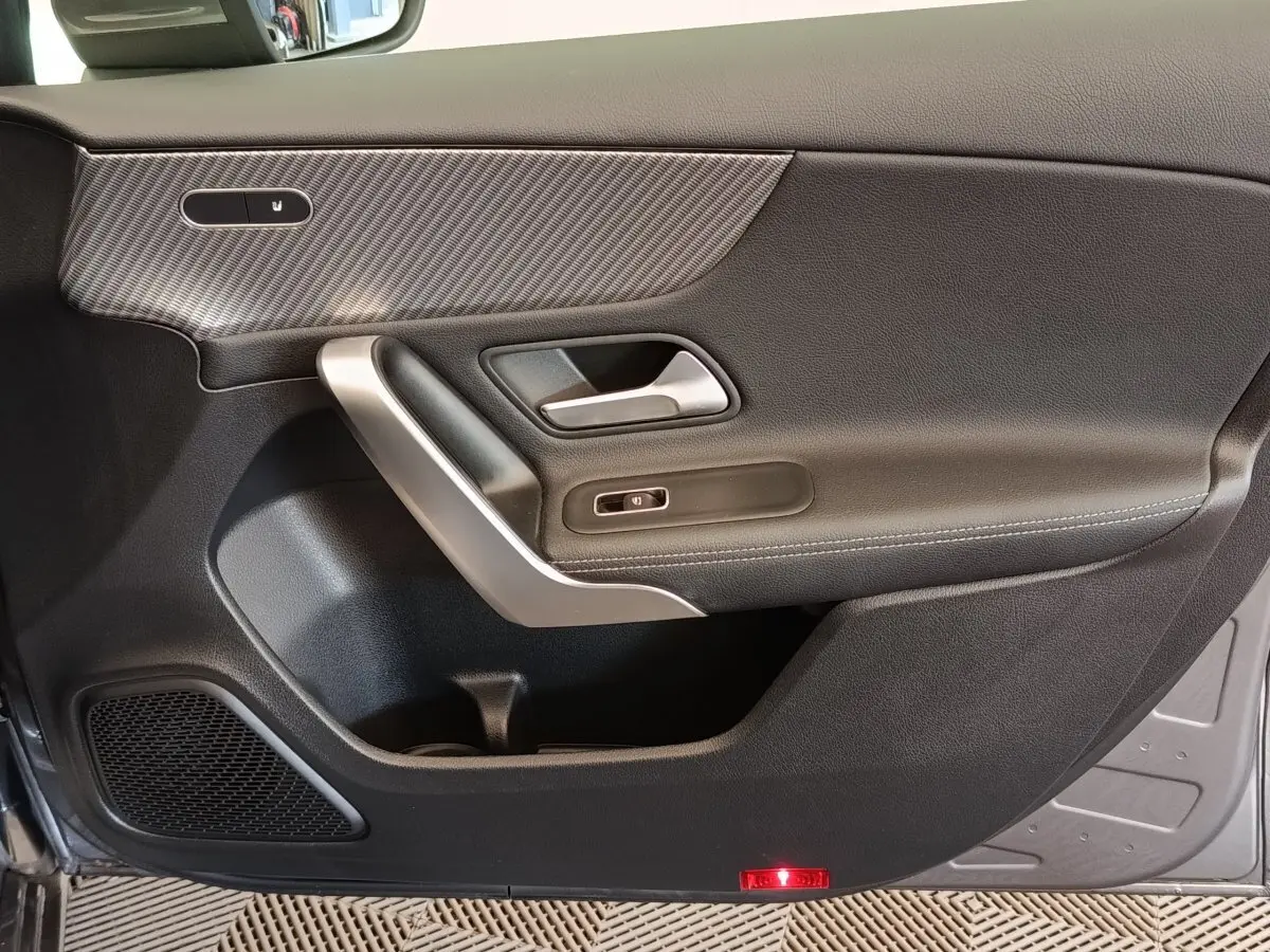Porte intérieure côté gauche de la Mercedes Classe A 250 e Hybrid gris foncé avec garniture carbone et poignée argentée.