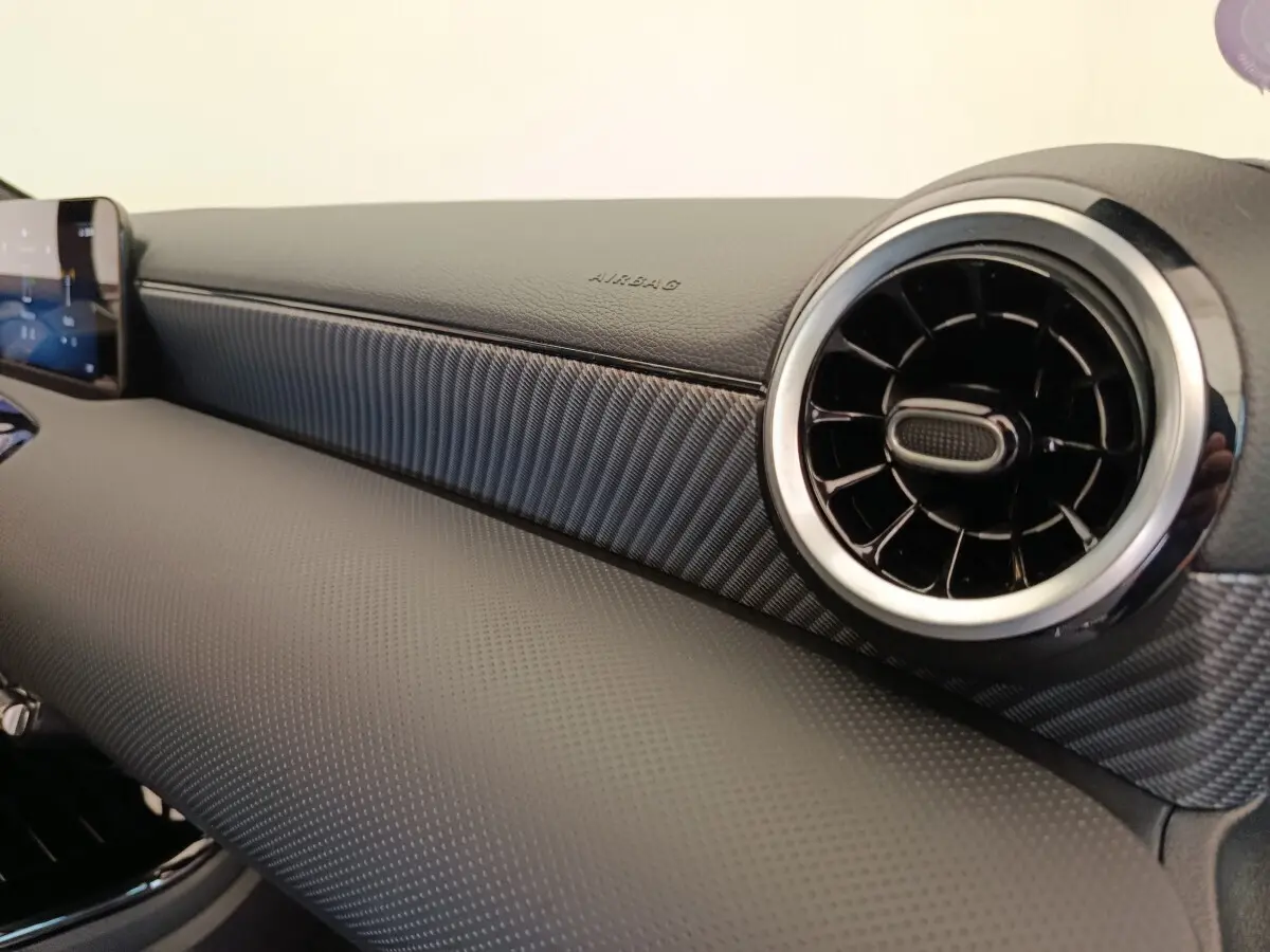 Détail du tableau de bord noir avec sortie d'air ronde chromée et écran tactile dans une Mercedes Classe A 250 e Hybrid 2024.