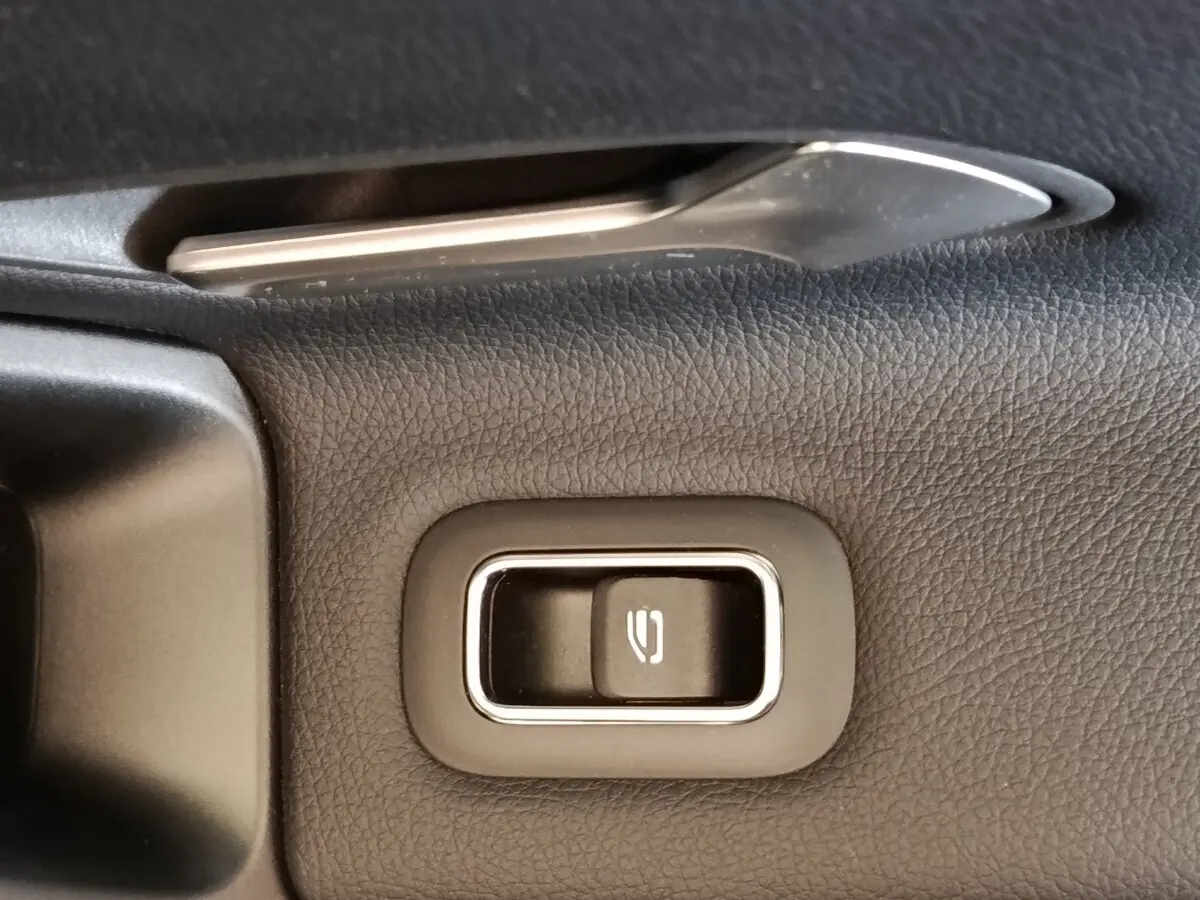 Gros plan sur la commande de lève-vitre électrique côté conducteur, entourée de cuir noir texturé.