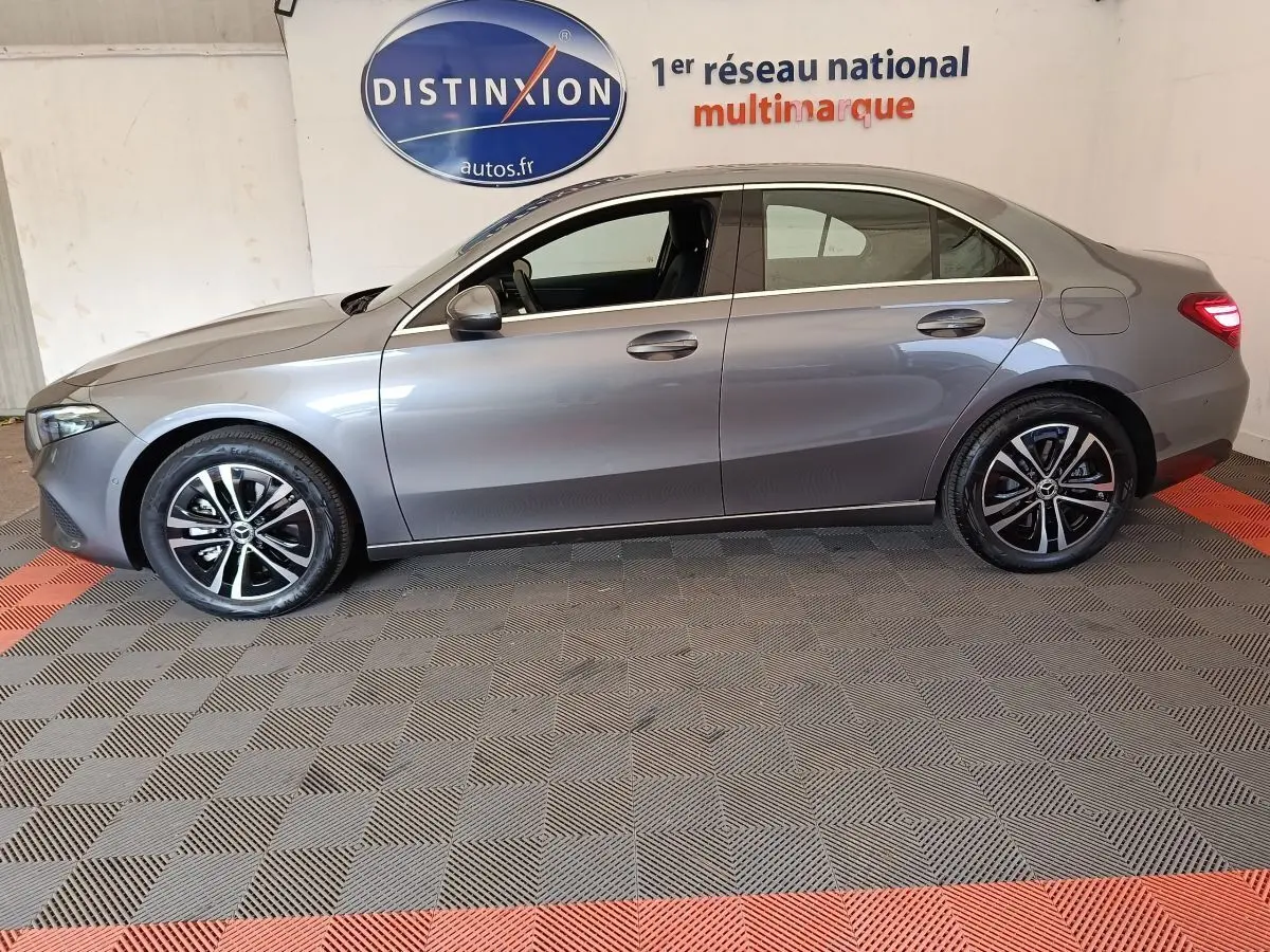 Profil droit d'une Mercedes Classe A 250 e Hybrid gris foncé, avec jantes alliage et feux arrière allumés en intérieur showroom.