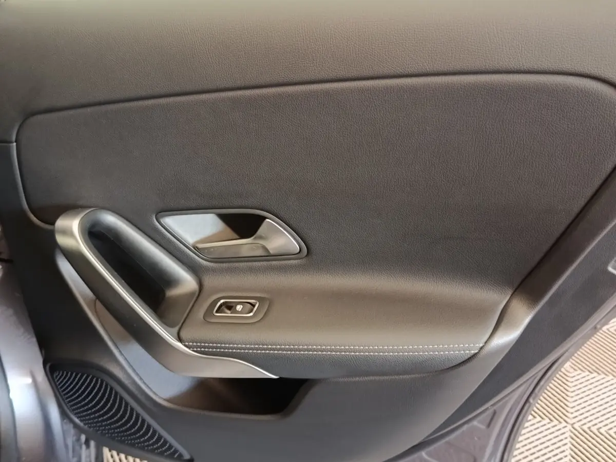 Gros plan sur la garniture intérieure de porte noire avec poignée argentée et bouton de commande de vitre, côté conducteur.