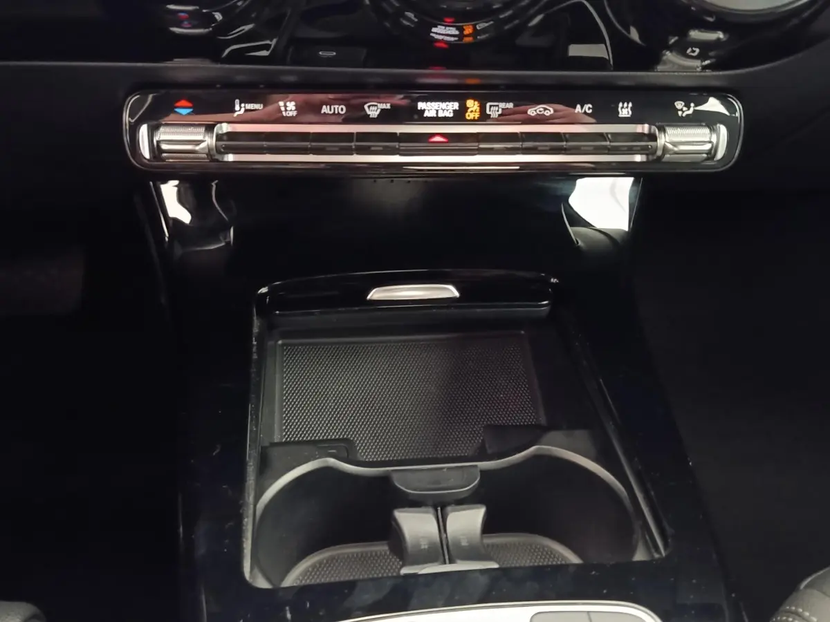 Vue rapprochée de la console centrale noire brillante avec commandes climatisation tactile et porte-gobelets d’une Mercedes Classe A 250 e hybride 2024.