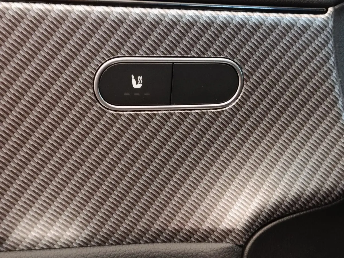 Détail du bouton de siège chauffant sur la garniture intérieure en fibre de carbone grise d'une Mercedes Classe A 250 e Hybrid 2024.