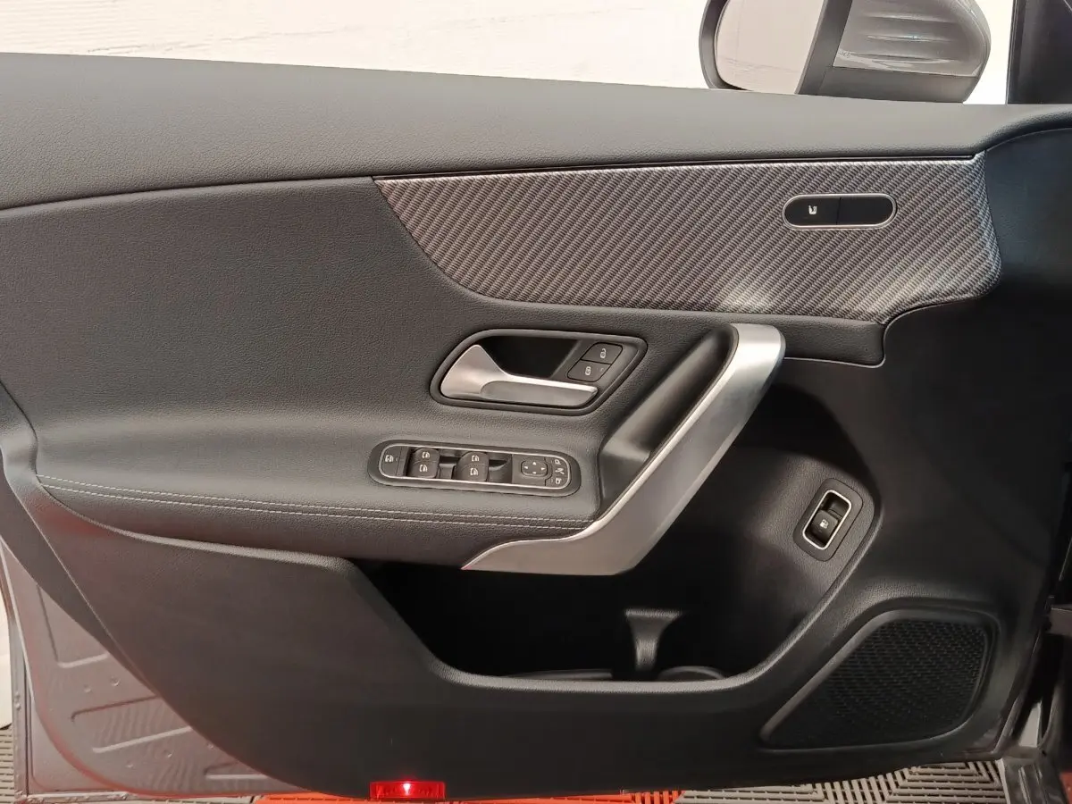 Vue intérieure côté gauche de la porte d’une Mercedes Classe A 250 e Hybrid gris foncé avec insert carbone et commandes électriques.