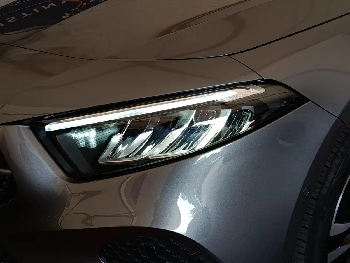 Gros plan sur le phare avant droit d’une Mercedes Classe A 250 e Hybrid gris foncé 2024, détails LED visibles.