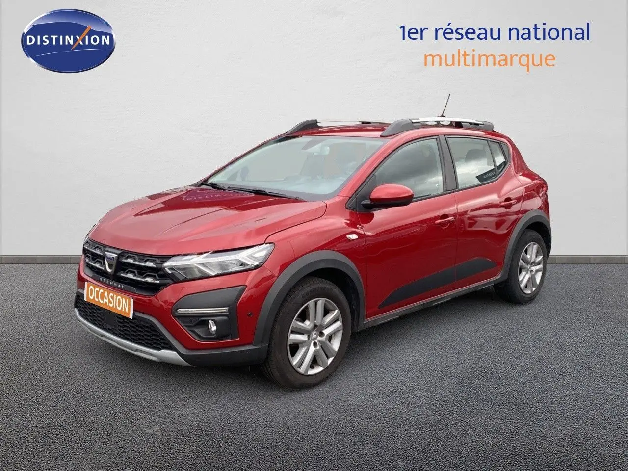 Dacia Sandero Stepway rouge fusion métal en 3/4 avant droit, avec protections noires et barres de toit visibles.