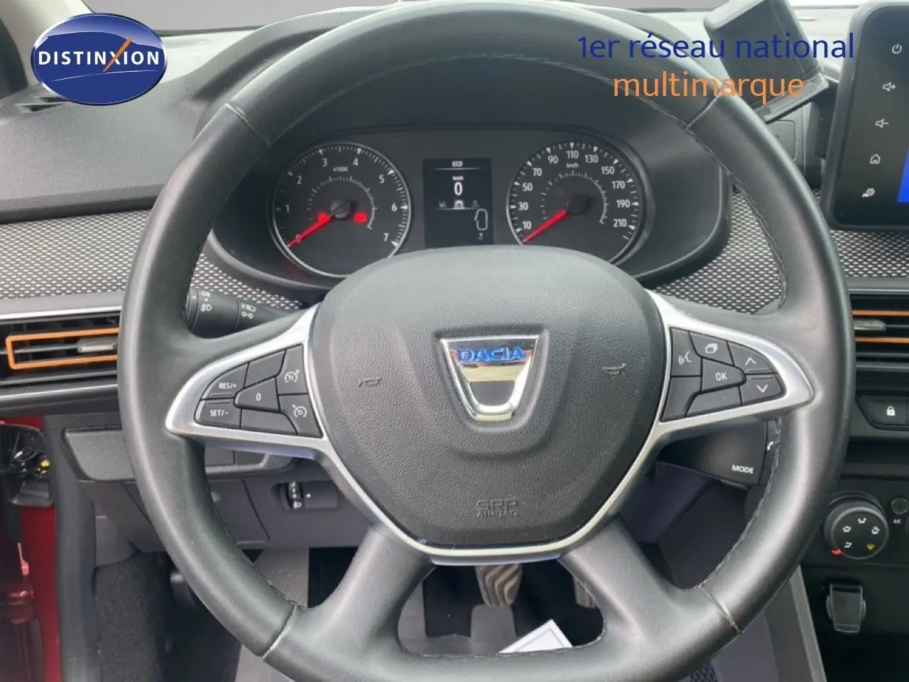 Vue rapprochée du volant noir de la Dacia Sandero 2022 avec tableau de bord et commandes visibles, intérieur rouge partiel.
