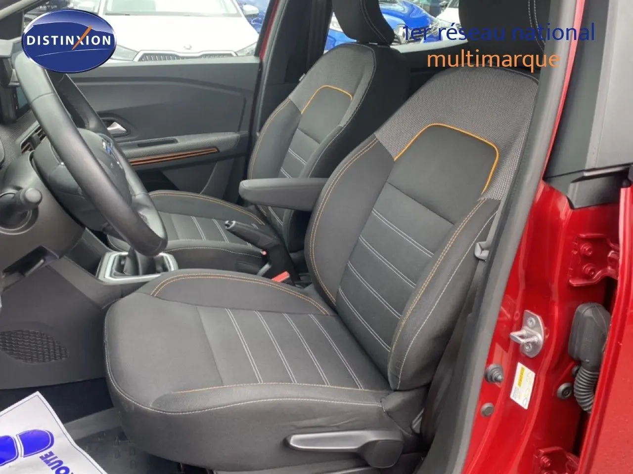 Vue intérieure côté gauche des sièges avant noirs avec surpiqûres orange d'une Dacia Sandero rouge fusion métal 2022.