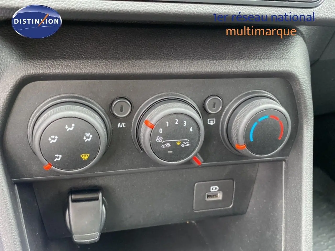 Gros plan sur les commandes de climatisation de la Dacia Sandero rouge fusion, avec réglages manuels et port USB visible.