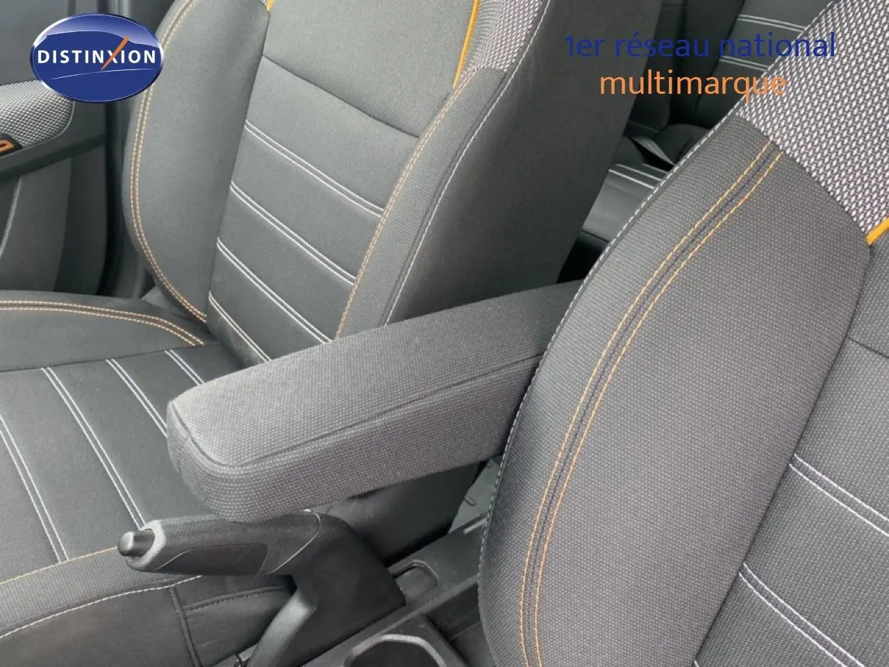 Gros plan sur l'accoudoir central et les sièges avant en tissu gris avec surpiqûres orange du Dacia Sandero Stepway 2022.