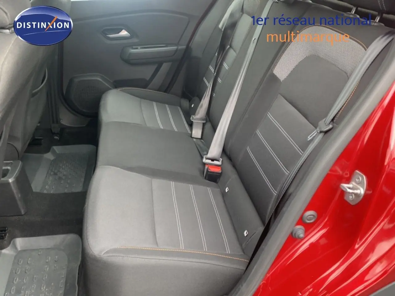Vue intérieure arrière côté droit du Dacia Sandero rouge fusion, montrant les sièges tissu gris avec surpiqûres orange.