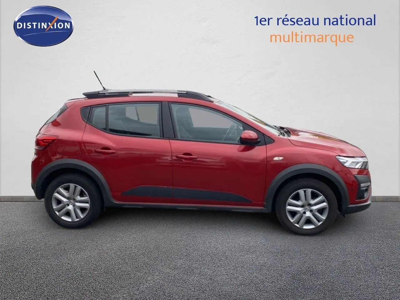 Vue latérale droite d'une Dacia Sandero Stepway rouge fusion métal avec barres de toit et protections noires.