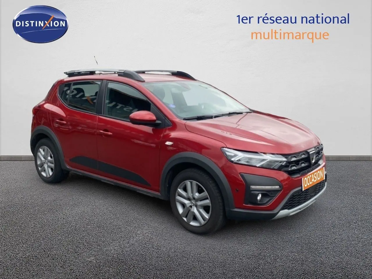 Vue 3/4 avant gauche d'une Dacia Sandero Stepway rouge fusion métal avec protections noires et barres de toit.