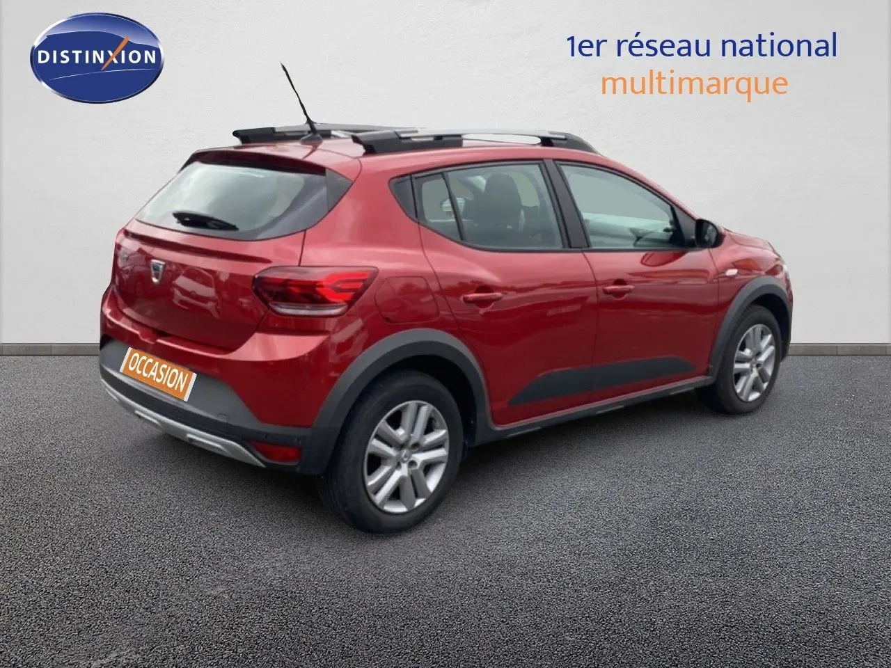 Vue 3/4 arrière droite d'une Dacia Sandero Stepway rouge fusion métal avec barres de toit et protections noires.