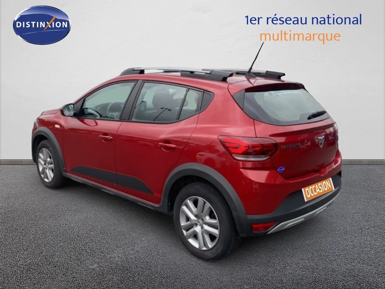 Vue 3/4 arrière droite d'une Dacia Sandero Stepway rouge fusion métal avec barres de toit et protections noires.