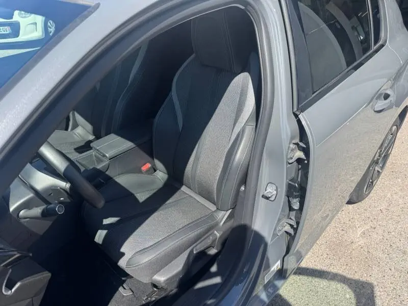Vue intérieure côté conducteur d'une Peugeot 308 gris 2025, siège réglable en hauteur avec accoudoir central.