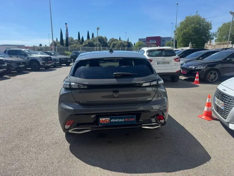 Vue arrière d'une Peugeot 308 Hybrid gris 2025 avec feux étirés et double sortie d'échappement, stationnée en extérieur.