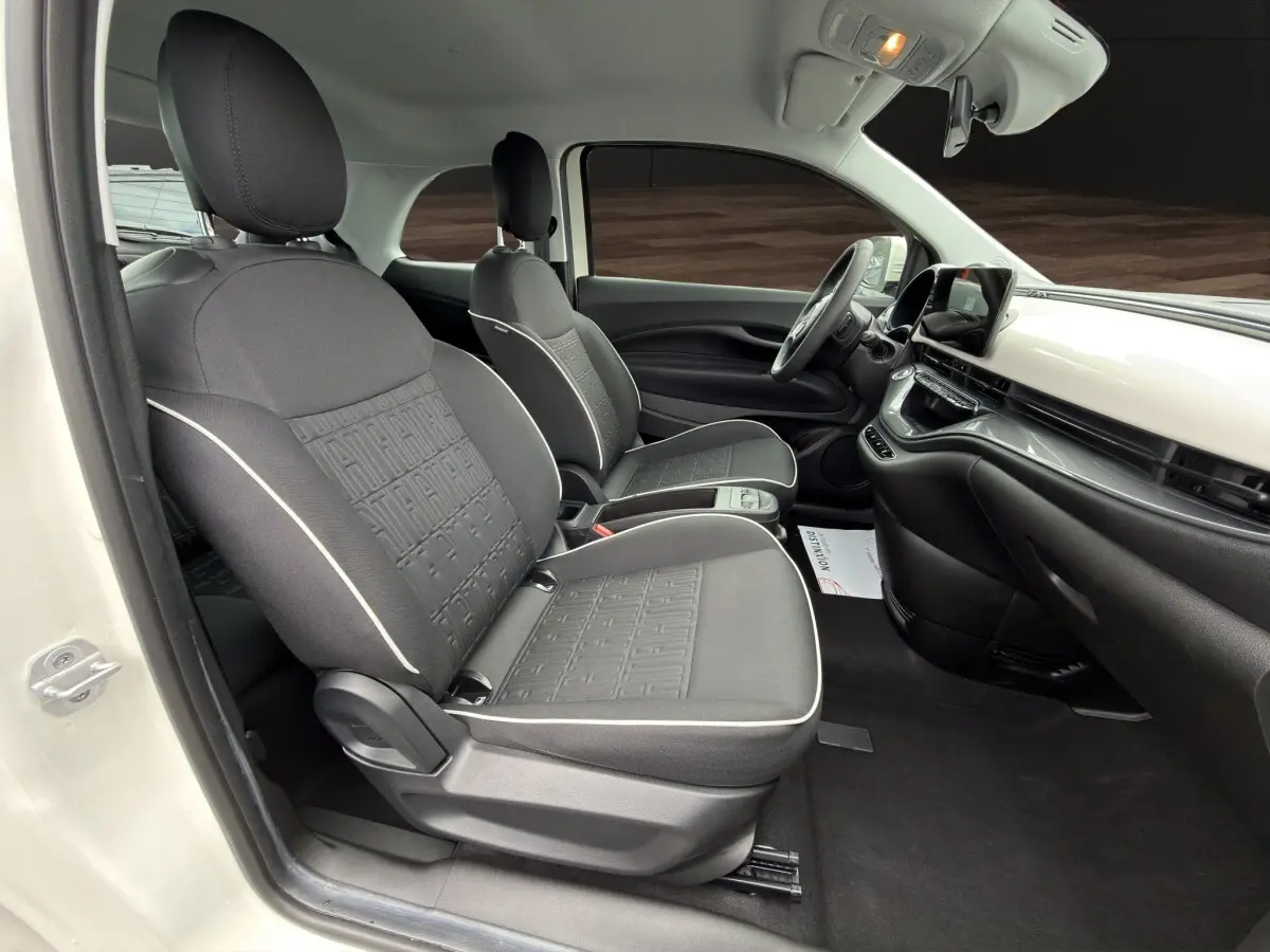 Vue intérieure côté conducteur de la Fiat 500 blanche 2023, sièges noirs avec surpiqûres claires et tableau de bord épuré.