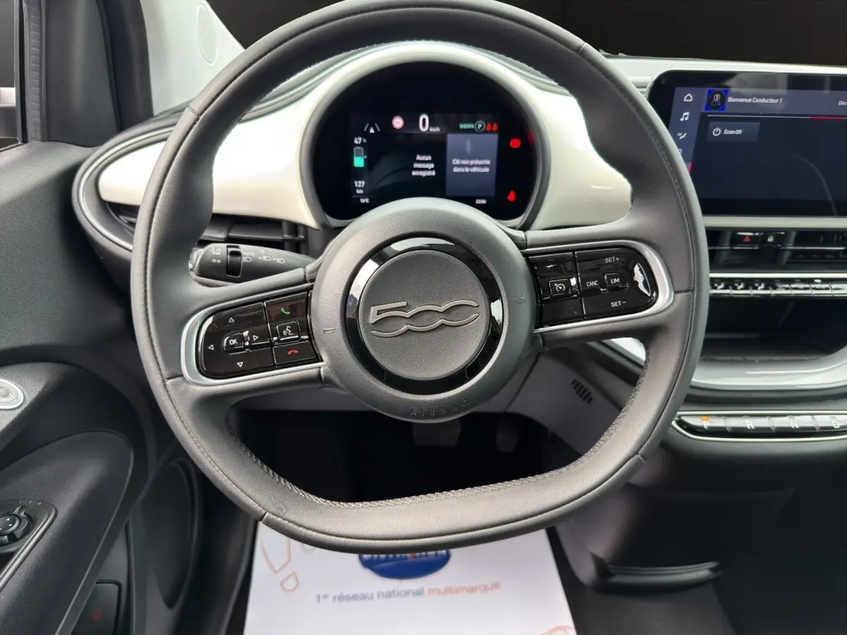 Vue rapprochée du volant cuir noir et du tableau de bord blanc de la Fiat 500 électrique 2023 avec écran tactile central.