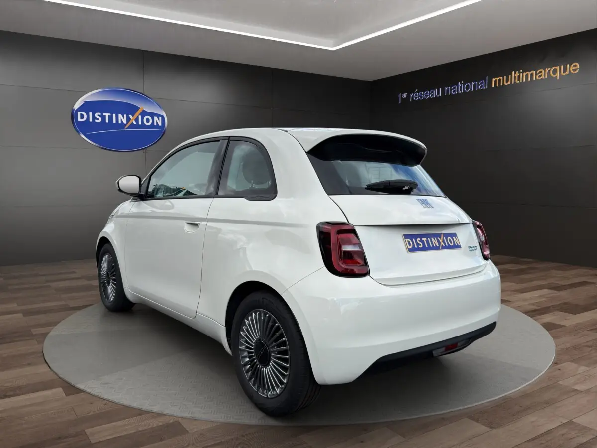 Vue 3/4 arrière droite d'une FIAT 500 électrique blanche avec jantes alu spécifiques et toit noir contrasté.