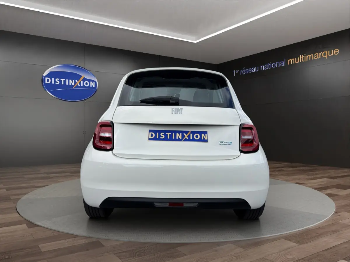 Vue arrière d'une Fiat 500 blanche électrique 2023 dans un showroom avec logo Distinxion en arrière-plan.