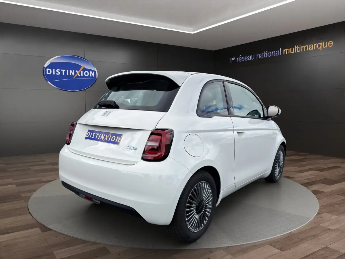 Vue 3/4 arrière droite d'une FIAT 500 électrique blanche avec jantes alu stylisées en exposition showroom.