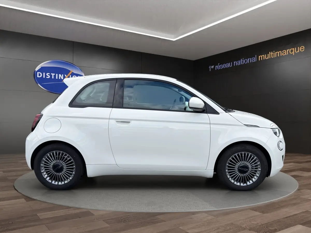 Profil droit de la FIAT 500 électrique blanche 2023 avec jantes alu et toit spoiler en showroom.
