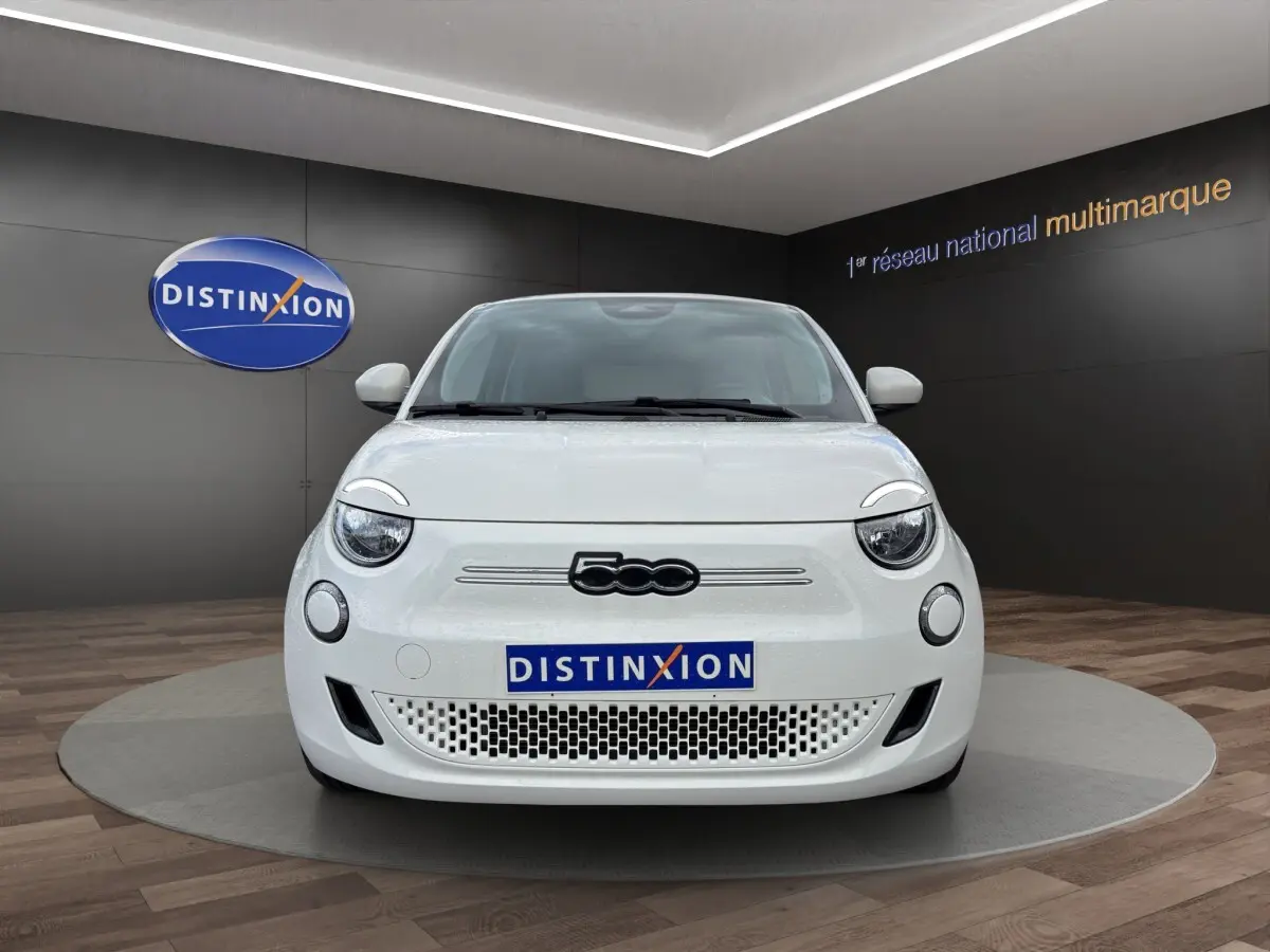 Vue frontale d'une FIAT 500 électrique blanche 2023 avec logo 500 noir et plaque Distinxion en showroom.