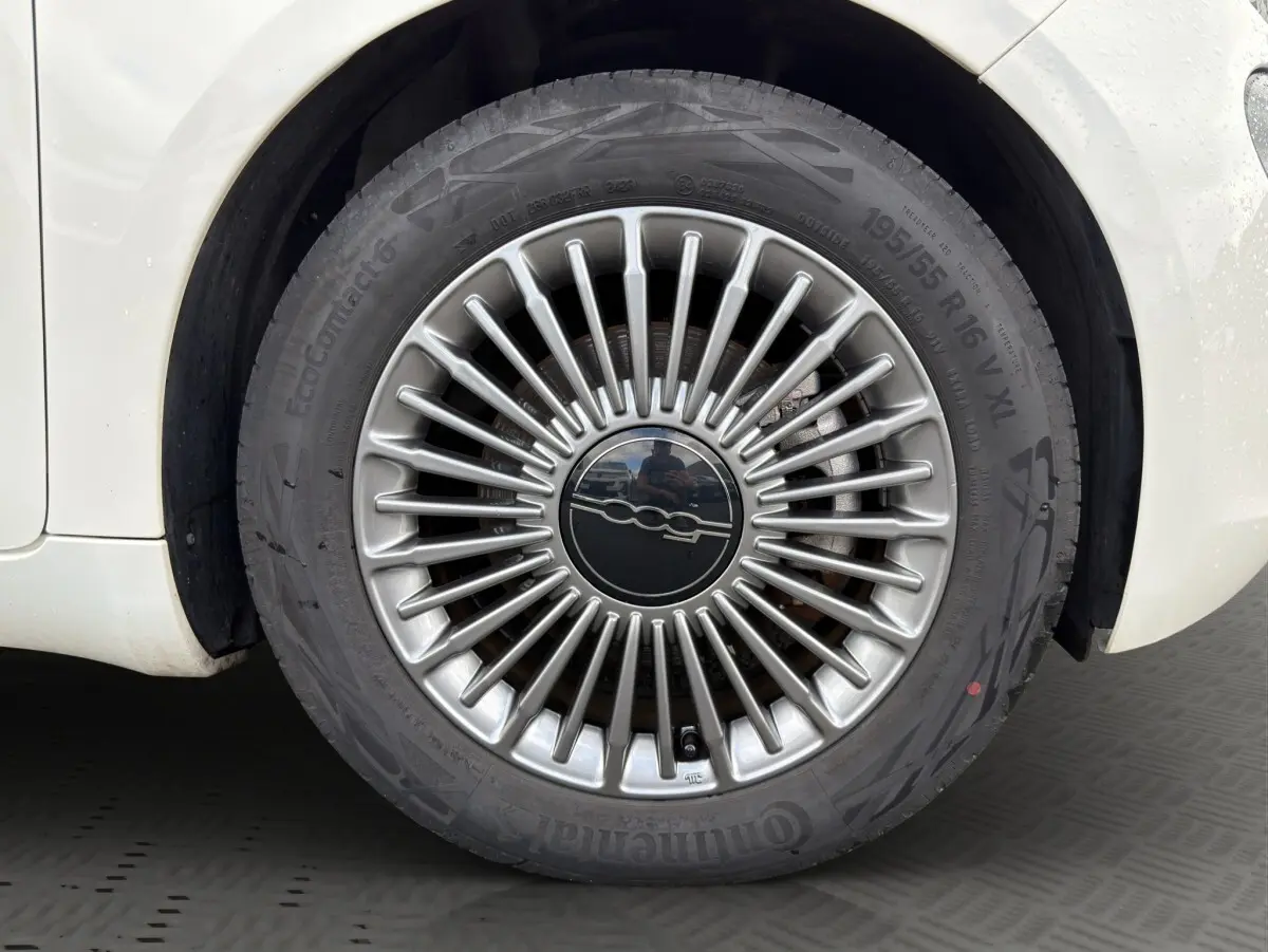 Gros plan sur la jante alu argentée au design rayonné d’une FIAT 500 blanche électrique, côté arrière droit.