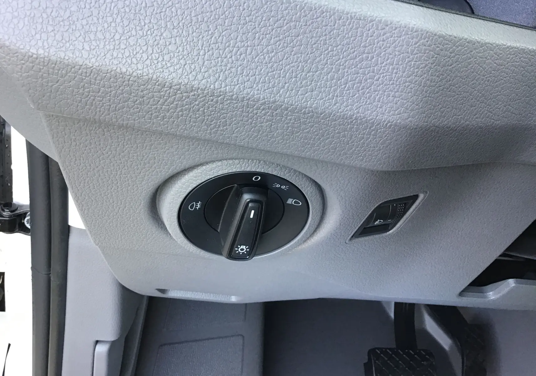 Gros plan sur le bouton de commande des phares dans l'habitacle gris clair du Volkswagen Crafter Fourgon blanc.