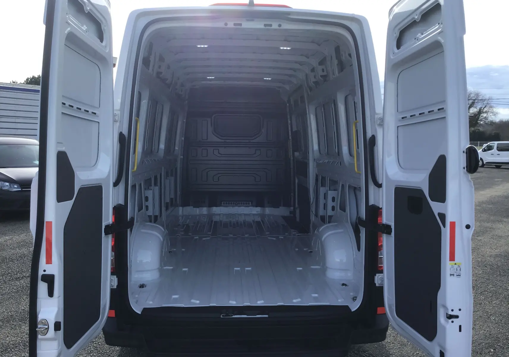 Vue arrière du Volkswagen Crafter Fourgon blanc 2024 avec portes ouvertes montrant la grande capacité de chargement vide.