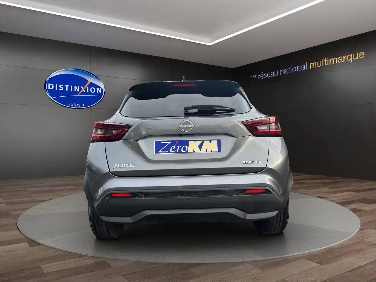 Vue arrière d'un Nissan Juke gris squale hybride, avec feux LED et logo Zero KM visible sur fond showroom.