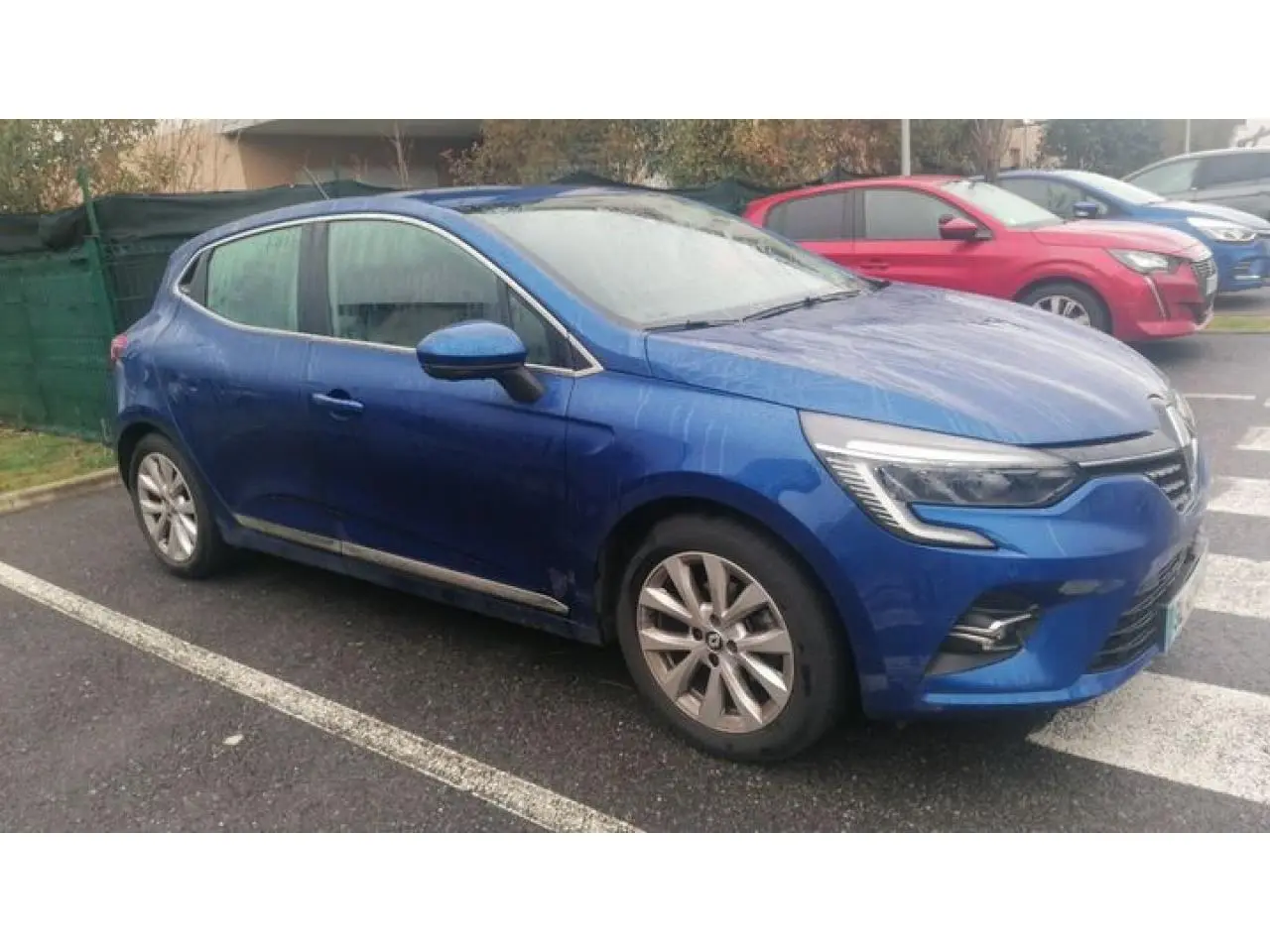 Renault Clio 2021 Bleu Iron vue de profil côté gauche, garée sur un parking extérieur par temps humide.