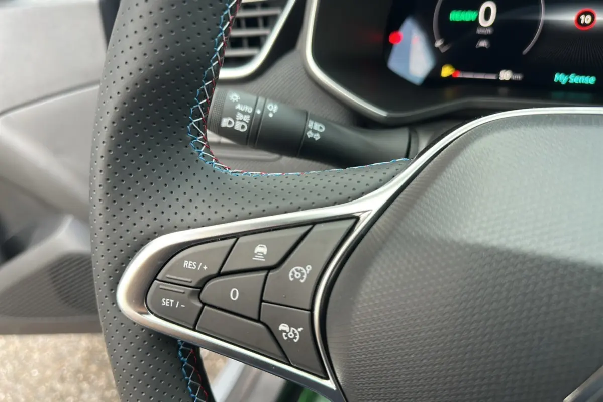 Gros plan sur les commandes au volant cuir perforé avec surpiqûres bleues de la Renault Clio V E-Tech 145 Esprit Alpine Bose.