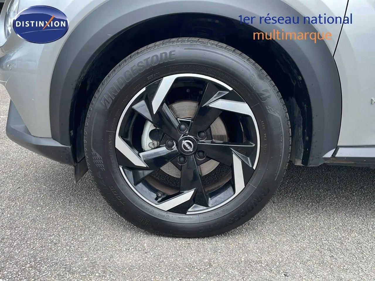 Gros plan sur la roue avant gauche du Nissan Juke gris perle métal, avec jante alliage noire et argentée au design moderne.