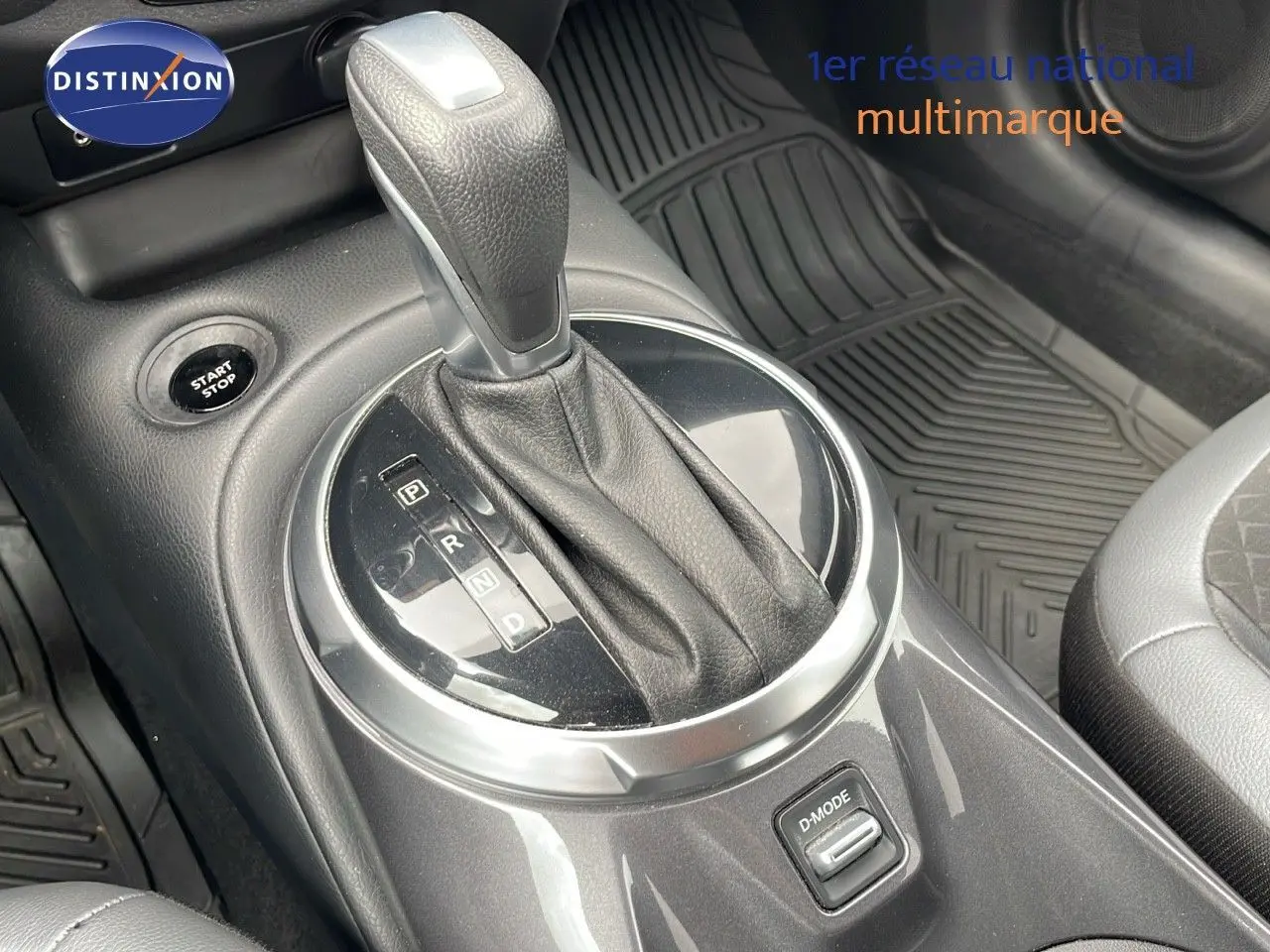 Le levier de vitesse automatique du Nissan Juke Hybrid gris perle, avec bouton start/stop et tapis caoutchouc visible.