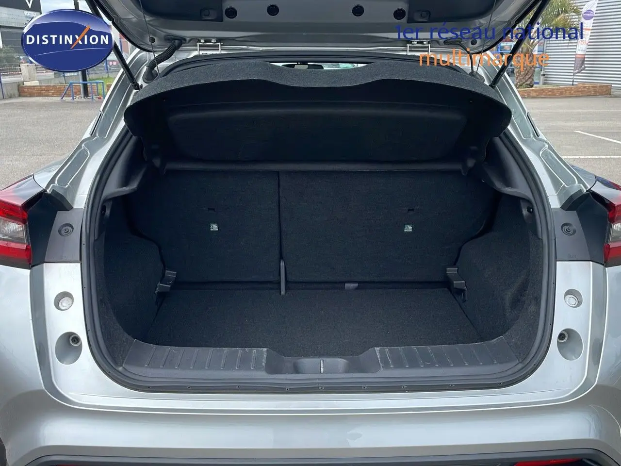 Coffre ouvert d'un Nissan Juke Hybrid gris perle métal, vue arrière mettant en valeur l'espace de chargement vide.