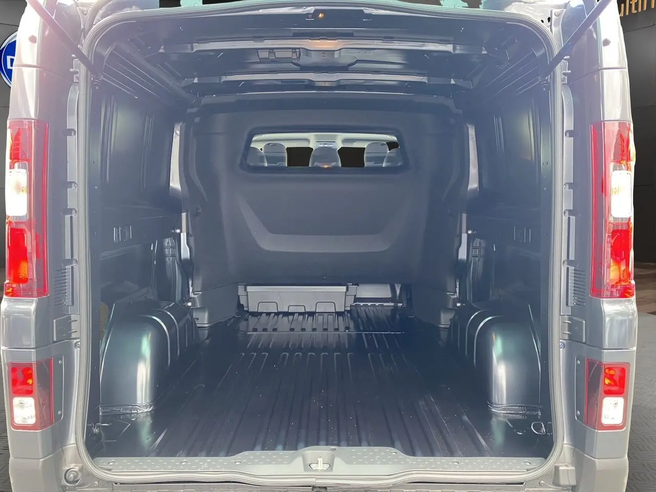Vue arrière du Renault Trafic cabine approfondie gris comète, montrant l'espace de chargement vide et les feux arrière allumés.